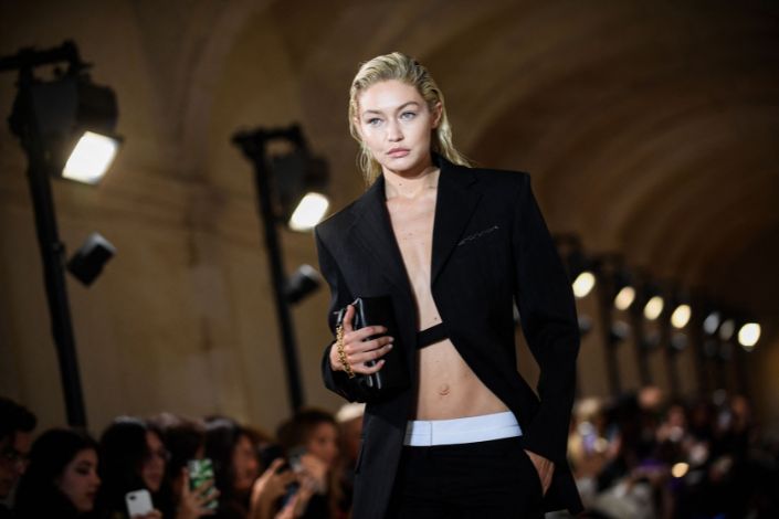 Gigi Hadid walks as a model in a fashion show wearing an open black blazer. 