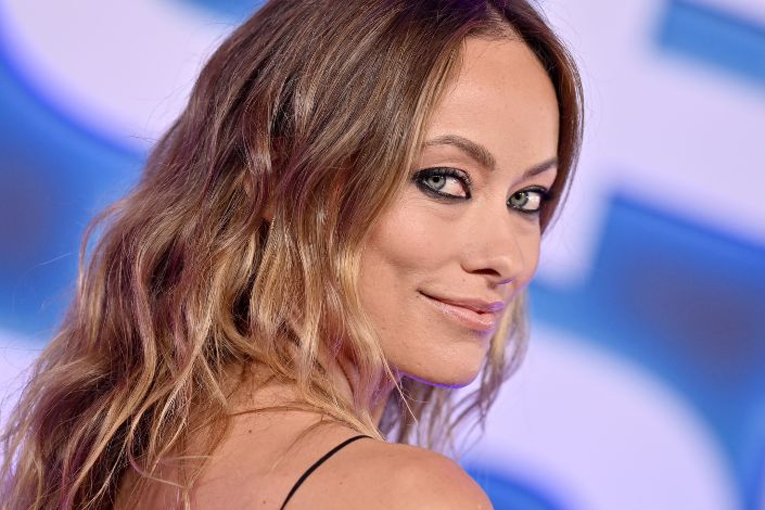 A close up image of Olivia Wilde looking over her shoulder while smiling at camera. 