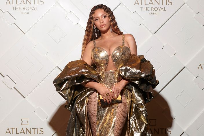 Beyoncé posing in a shimmery gold dress with a matching shoulder wrap. 