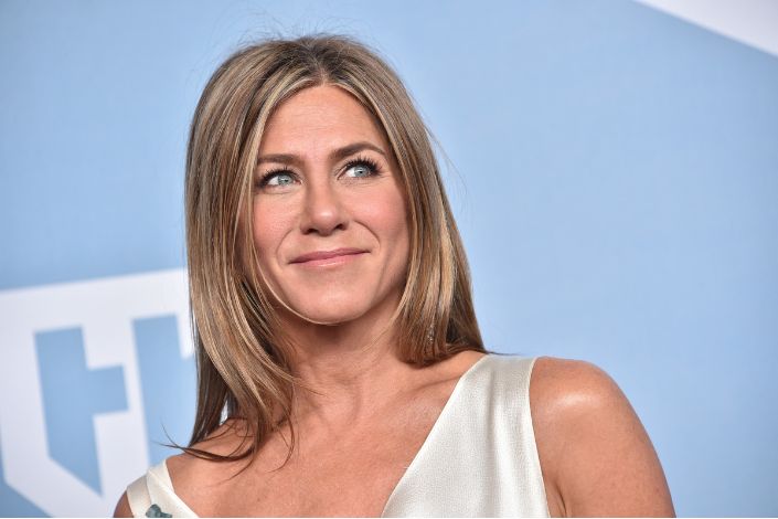 Jennifer Aniston smiles at an event while wearing an ivory dress.