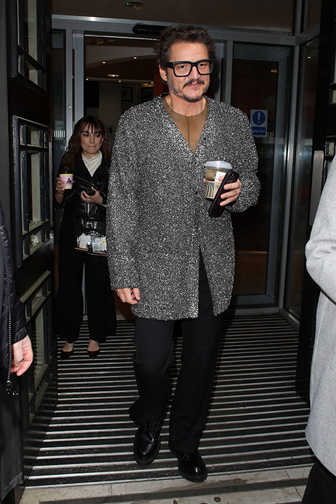 Pedro Pascal holds a coffee while wearing a sparkly grey cardigan