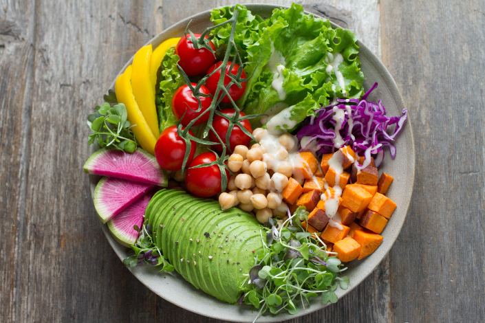 A bowl of fruits and vegetables including avocado, leafy greens and sweet potato