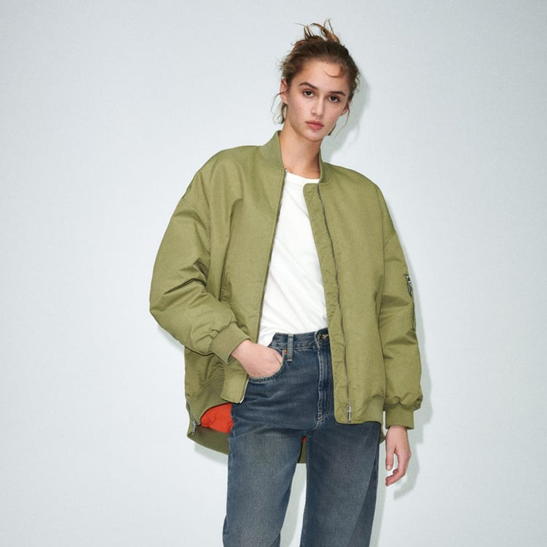 a young white woman with her hair pulled back wears a bomber jacket