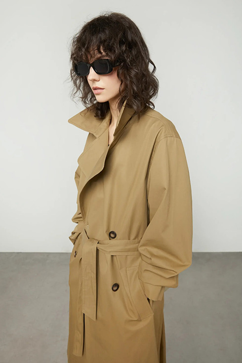 a woman with glasses wearing a tan belted trench coat