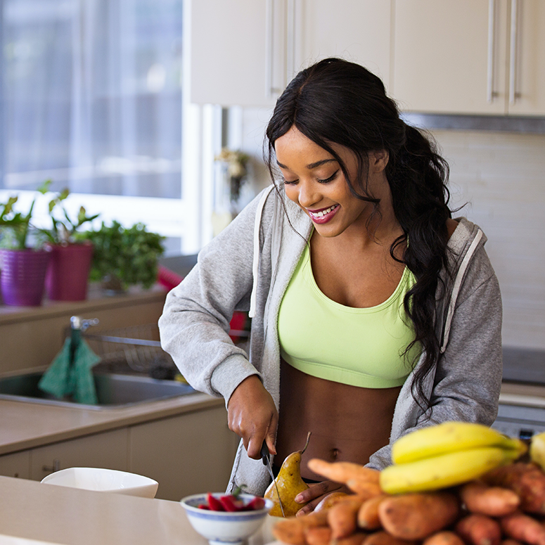 a young woman with long black hair in workout gear, standing in her kitchen chopping food
