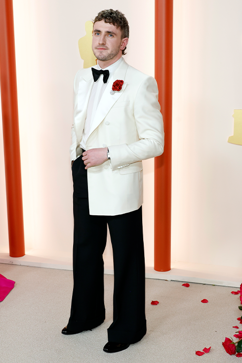 Paul Mescal in bell-bottomed pants and a white tuxedo jacket with a rose on his lapel