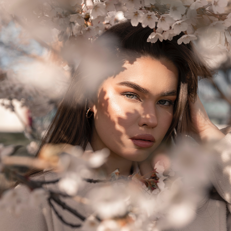 A woman with natural makeup looking through a cherry blossom tree