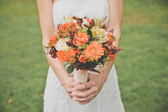 a closeup of an orange floral arrangement, held by a bride