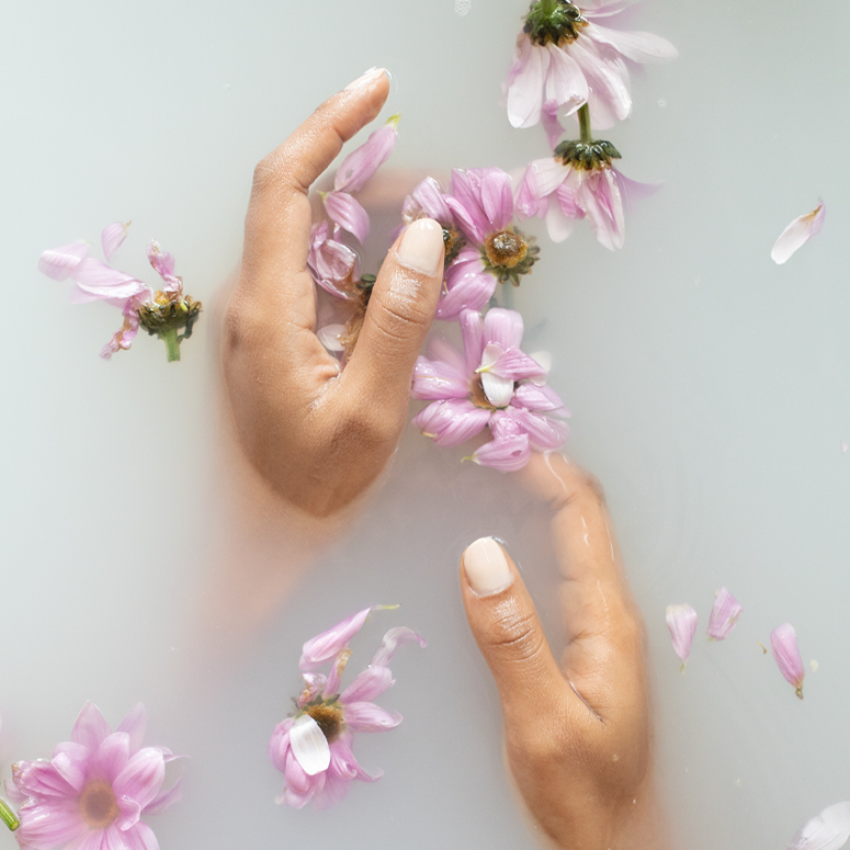 Two hands with an off-white manicure in hazy water with pink flowers