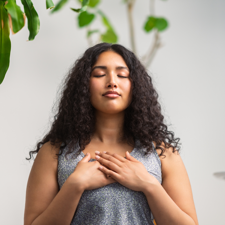 Woman with curly hair with eyes closed and hands on chest.
